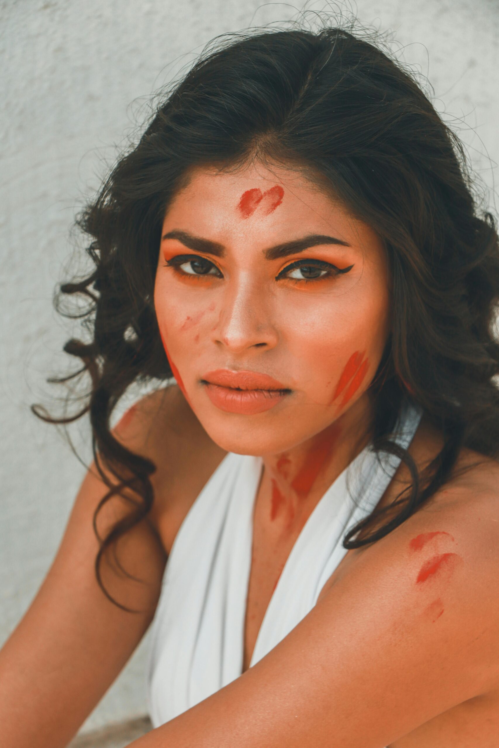 Portrait of a South Asian woman with red paint accents and bold makeup.